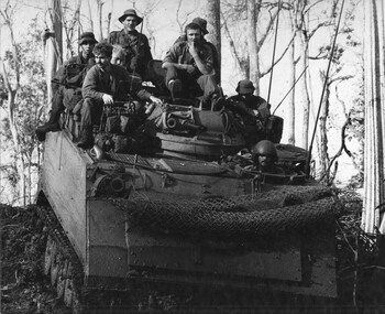 A black and white photograph of seven diggers sit atop an APC with the APC driver in position.