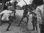 A photograph of In Baria, Phuoc Tuy Province two Vietnamese boys play a martial arts games using sticks. A younger brother and sister look on