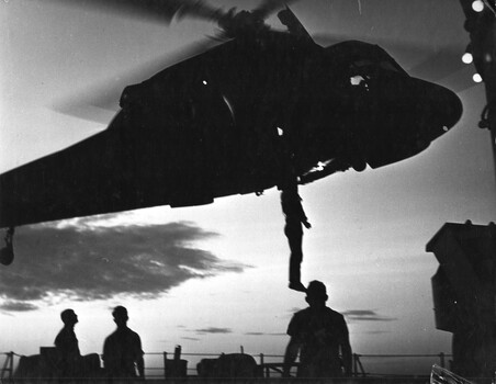 A photograph of an American 6th Fleet helicopter delivers crew members by winch from HMAS Hobart to their ship.