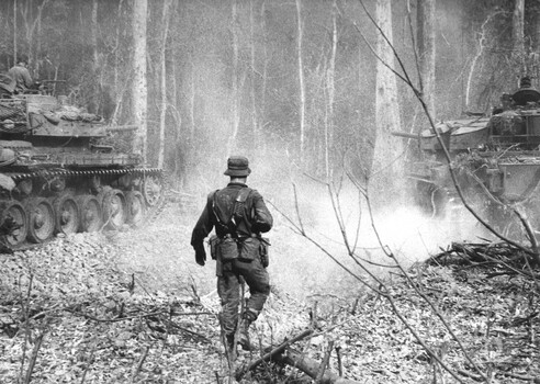 A photograph of a digger from 2 Platoon, A Coy 1 RAR advances with Centurian tanks of 1 Troop, C Squadron, 1st Armoured Regiment. 