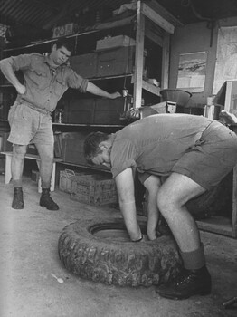 A photograph of Diggers from the transport section at the 1st Australian Field Hospital, conduct repairs to a tyre from an ambulace. 