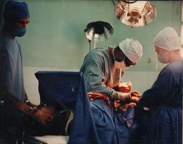 A coloured photograph - At the 1st Australian Field Hospital a surgical team works on a wounded patient. 