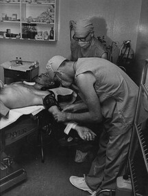 A photograph of Cpl Alex (Chuck) Berry, while the Anaeshetists looks on, in the operating theatre at 1st Australian Field Hospital. 