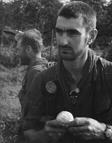 A tired and dirty Pte Jack Higgins about to enjoy an orange while his boss Maj Jake O'Donnell MC, 7 RAR  watches his company. 