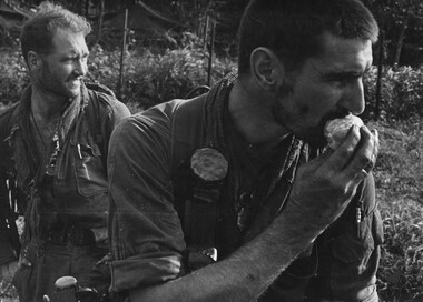 A tired and dirty Pte Jack Higgins enjoys a peeled orange, while his boss Maj Jake O'Donnell MC, A Company 7 RAR watches his company.