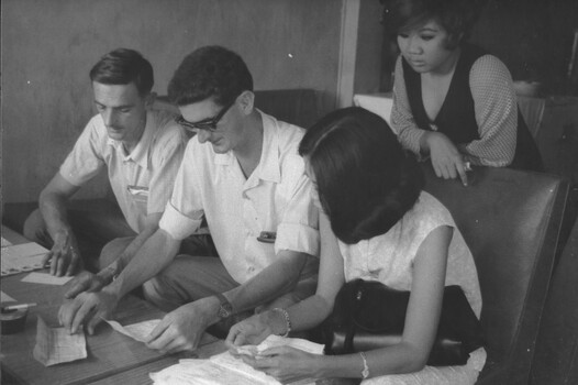 A photograph of plain clothes Military Police with the aid of two female Vietnamese interpreters study confiscated and captured documents.