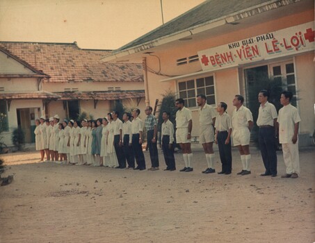 A coloured photograph of the Staff of Benh Vien Le Loi hospital stand to attention at the front of the hospital