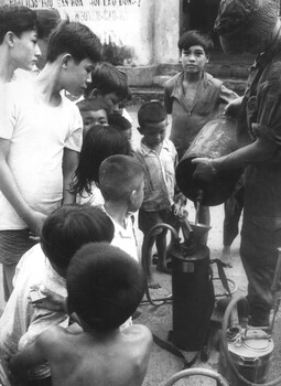 Digger from 1st Aust Field Hygiene Unit with interested children while he fills his backpack spray unit to spray the Long Dien Village. 