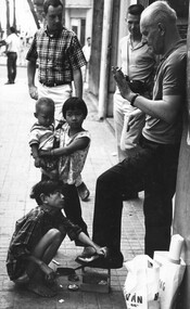 An American servicemen and civilians in Saigon argue with a Vietnamese 'Shoe Black' as he cleans one of their shoes.  