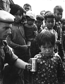 2Lt Mike Meehan of 161 (Indep) Recce Flight attempts to entice a little Vietnamese girl to have a can of chilled chocolate milk.