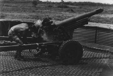 A digger reaches down to grab the spent shell casing on a 105mm Italian Pack Howitzer during a fire mission from the 1st ATF Base.