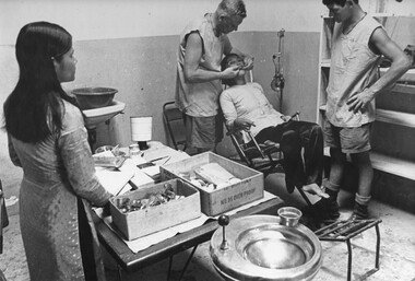 At 1st Australian Field Hospital, a dentist works on a Vietnamese patient while a dental assistant and female Vietnamese aide look on. 