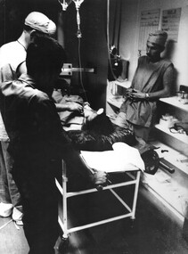 Medics watched by a South Vietnamese Army Intelligence Officer, prepare a wounded enemy VietCong soldier for treatment at 1st Australian Field Hospital. 