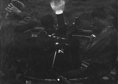 A photograph of the crew of a New Zealand mortar, mounted inside an Australian Australian Personnel Carrier, cover their ears against the blast sound.