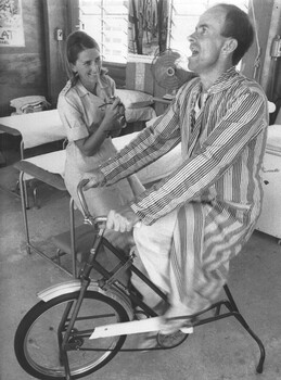 A RAAF inpatient at the 1st Australian Field Hospital Physiotherapy hut receives encouragement from the physiotherapist Lt Diane Skewes to try harder.