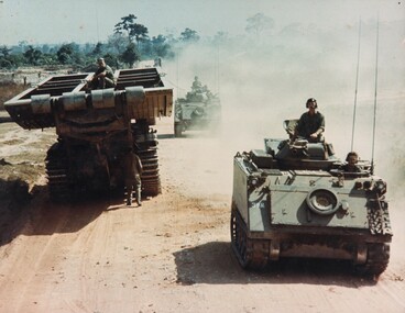 Two armoured personnel carriers (APC's)  pass a Centurian Tank Bridgelayer during Operation Matilda.