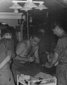 A black and white photograph of Capt Jack Bromley, 2 Field Ambulance Hospital, Nui Dat removes shrapnel from the neck of an SAS Digger 