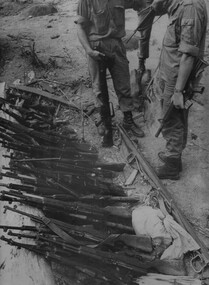 The CO of 6 RAR/NZ (ANZAC) Lt Col David Butler, along his Radio Operator and Intellegence Officer inspects the weapons found in the underground cache.