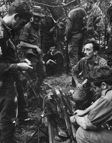 A captured NVA/VC looks on as Diggers inspect the weapons found in the large underground cache at the K76A Hospital.