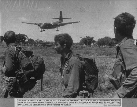 A photograph of Diggers of 5th Battalion, Royal Australian Regiment, watch a Caribou transport aircraft from 35 Squadron Royal Australian Air Force. 