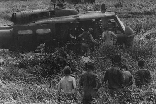 A photograph of Engineers with mine detectors watch a group of Diggers load a stretcher into an RAAF "Slick" helicopter. 