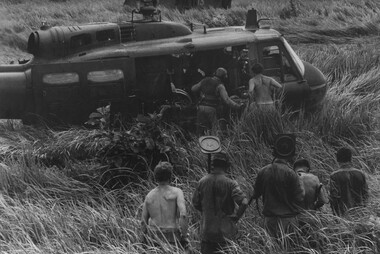 A photograph of Engineers with mine detectors watch a group of Diggers load a stretcher into an RAAF "Slick" helicopter. 