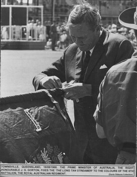 A photograph in Townsville, 18/08/1968. The Prime Minister of Australia, John Gorton fixes the "Long Tan Streamer" to the colours of 6th Battalion, The RAR.