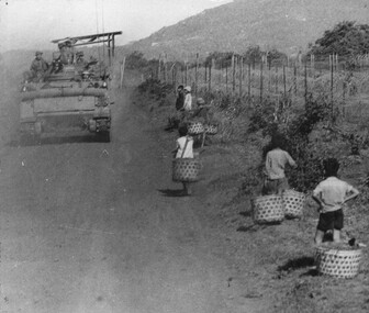 A photograph of APC's in Long Kahn Province roll past a group of Vietnamese children returning from collecting vegetables and herbs from their gardens. 