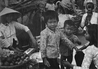 A photograph of Vietnamese children with their mothers, fruit and other types of food sellers on the footpath in Vung Tau City. 