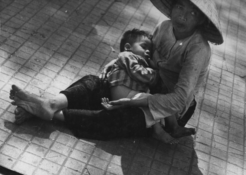A photograph of a deformed and seriously ill Vietnamese woman, beggar and her seriosly ill baby, working on the footpath in Saigon.