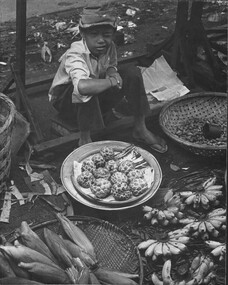 A black and white photograph of a young boy selling fruit and vegetables on the street.