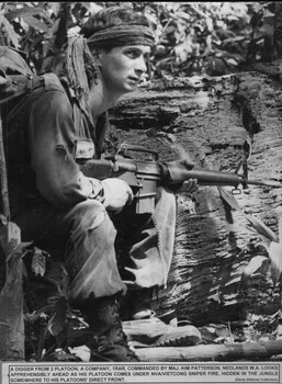 A photograph of a Digger from 2 Platoon, A Company, 1 RAR, looks apprehensibly ahead as his platoon comes under NVA/VietCong sniper fire. 