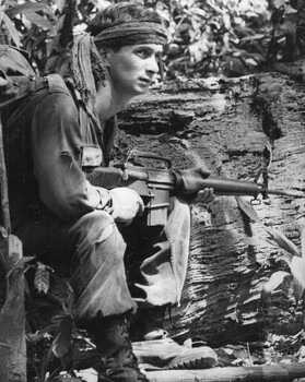 A photograph of a Digger from 2 Platoon, A Company, 1 RAR, looks apprehensibly ahead as his platoon comes under NVA/VietCong sniper fire. 