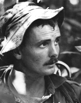 A photograph of a Digger from 2 Platoon, A Company, 1 RAR, looks aprehensively ahead as his platoon comes under NVA/VietCong sniper fire. 
