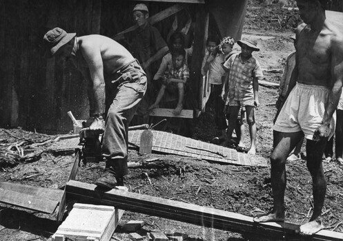 A Digger from 1st Australian Civil Affairs Unit stationed at 1st ATF Base assisted by a villager cuts timber for a house. 