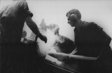 A Gunner of 104 Battery RAA at Fire Base Betty places a 105mm round in his gun his fellow Gunners check the gun sight. 