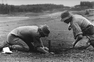 Capt Tony Eaton, the 1st ATF Artillery Intelligence Officer and Sgt Paul Butcher checks the impact area of a NVA/VietCong 107mm rocket for fragments.