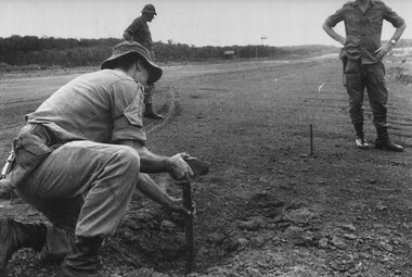 1st ATF Artillery Intelligence Officer Sgt Paul Butcher watched by Capt Tony Easton pound a stake into an impact area of a NVA/VietCong rocket. 