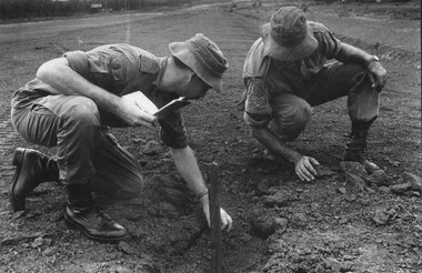 Capt Tony Eaton, the 1st ATF Artillery Intelligence Officer assisted by Sgt Paul Butcher checks the impact area of a NVA/VietCong 107mm rocket for fragments.