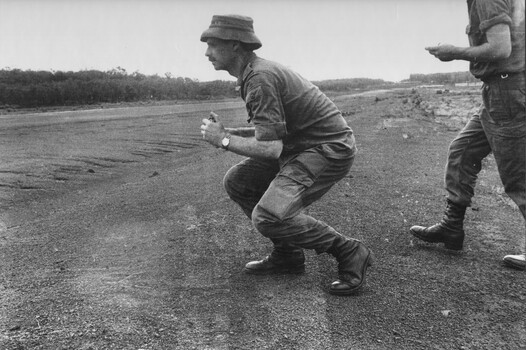 Capt Tony Eaton, 1st ATF Artillery Intelligence Officer crouches down to take a compass reading of the incoming direction of a NVA/VietCong 107mm rocket.