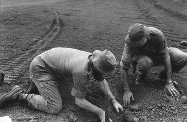 Capt Tony Eaton the 1st ATF Artillery Intelligence Officer assisted by Sgt Paul Butcher check an impact area of a NVA/VietCong 107mm rocket attack.