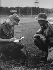 Two soldiers looking and taking note from a 107mm rocket hole