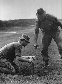 Two soldiers looking and taking note from a 107mm rocket hole