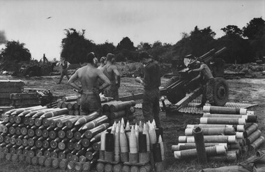 Several soldiers standing amongst artillery near a howitzer.