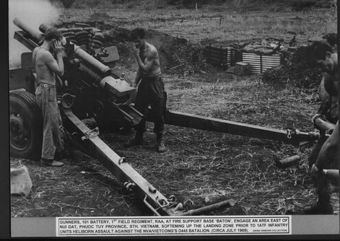 Two soldiers near a howitzer. One has his hands over his ears.