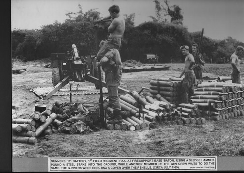 There are three soldiers standing amongst artllery shells. Also there is a soldier standing on round cylinders with another soldier on his shoulder.