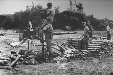 There are three soldiers standing amongst artllery shells. Also there is a soldier standing on round cylinders with another soldier on his shoulder.
