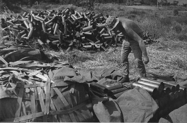 A photograph of a Gunner at the 1st Australian Task Force Base, Nui Dat, Phuoc Tuy Province, throwing a 105mm shell casing.