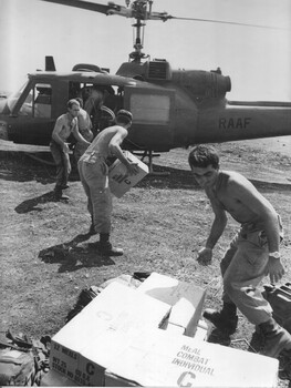 A photograph of Gunner Doug Blenkiron tossing cases of US Army C-Rations to another Gunner (wearing goggles) at 1 ATF Base, Nui Dat. 