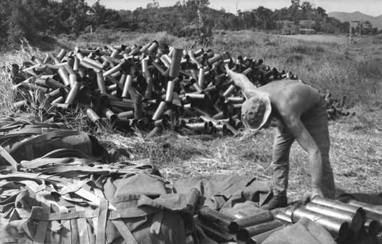 A photograph at a Fire Support Base, a digger sorting shell 105mm artillery shell casings. 